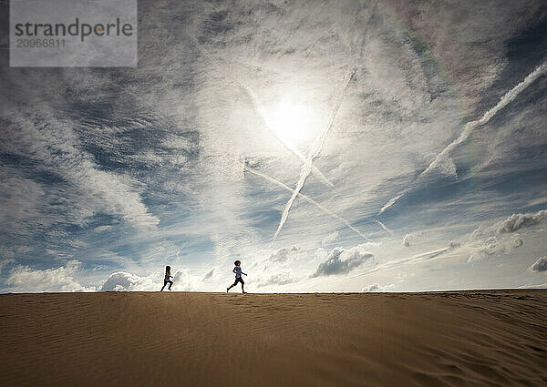 Young sisters running across sand dune under beautiful blue sky