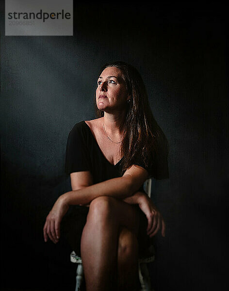 Portrait of woman sitting in chair dark room with dramatic light.