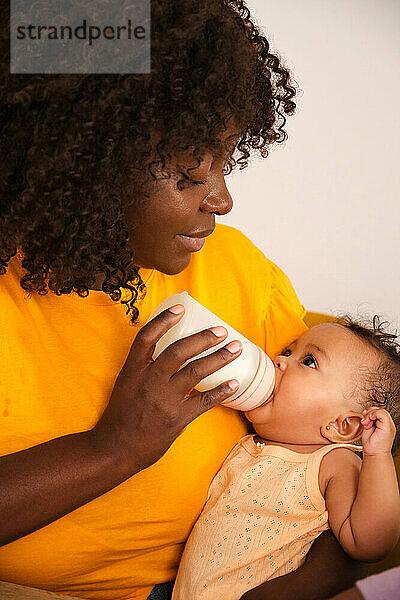 Loving mother bottle feeding her baby girl on white background