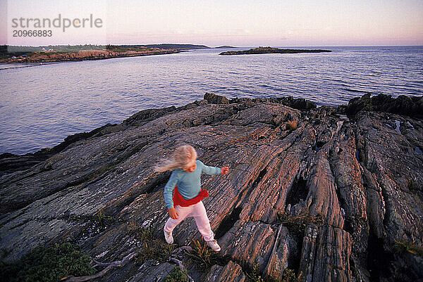 A young girl hops along rocky coast of Hermit Island  Maine.