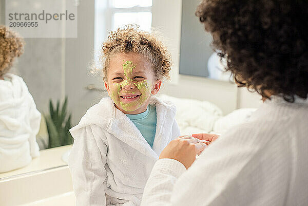 Little girl has green face mask on her face smiling