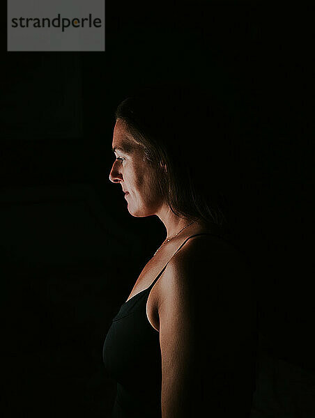 Portrait of attractive woman in dark room looking towards light.