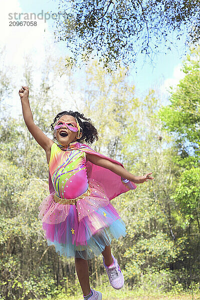 Young girl in superhero costume leaping with raised fist in a fo