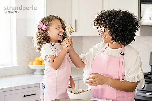 Sisters laughing together while holding a spoon with cookie dough