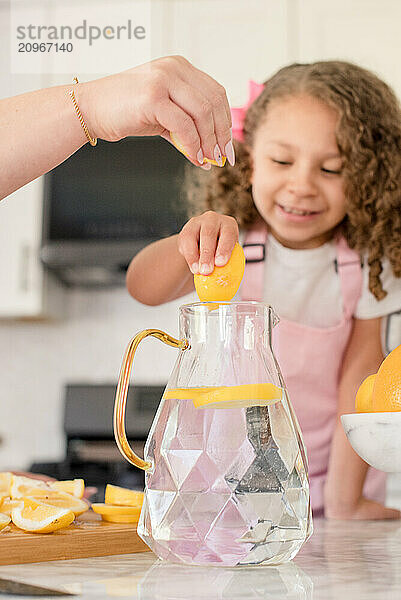 Little girl and mom squeezing lemon slices into pitcher