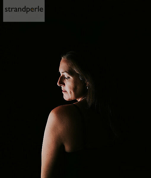 Portrait of attractive woman in dark room looking over shoulder.