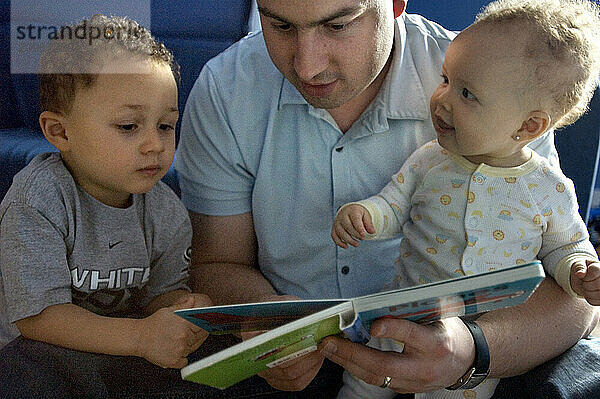 A father reads to his son and daughter.