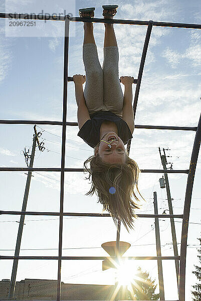 Happy young girl hanging from jungle gym sunny day