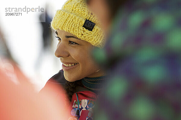 A young woman in ski gear laughs as she socializes with friends outdoors on the deck of a ski resort's bar and grill on a sunny day on the mountain.