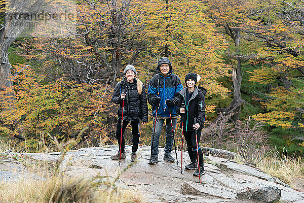 Three people are standing on a rocky hillside  wearing backpacks