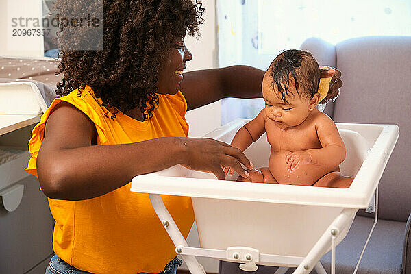 Mother washing her baby girl in a white bathtub