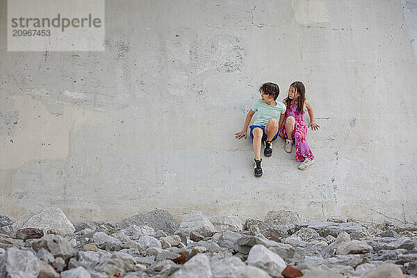 Two children sit on sloped cement wall in barren  urban landscape