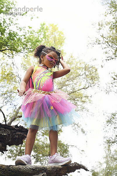 Young girl in superhero costume standing on a log  adjusting mas