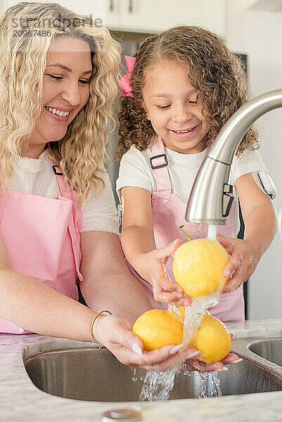 Mother and daughter washing lemons under the kitchen sink smiling