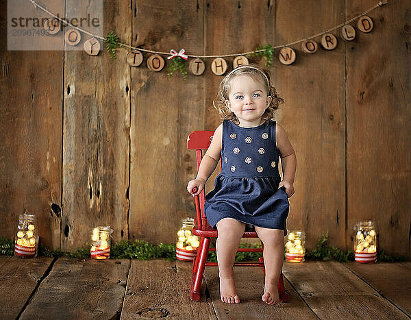 Beautiful toddler in blue dress wooden holiday backdrop lights