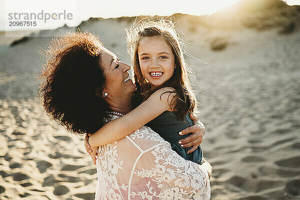 Grandma hugging kissing beautiful grandchild girl at beach