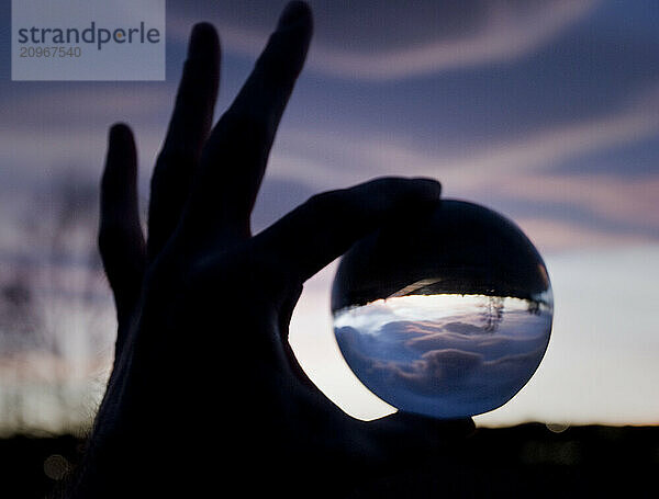 A sihouetted hand holds a crystal ball inverting a Denver  Colorado sunset.