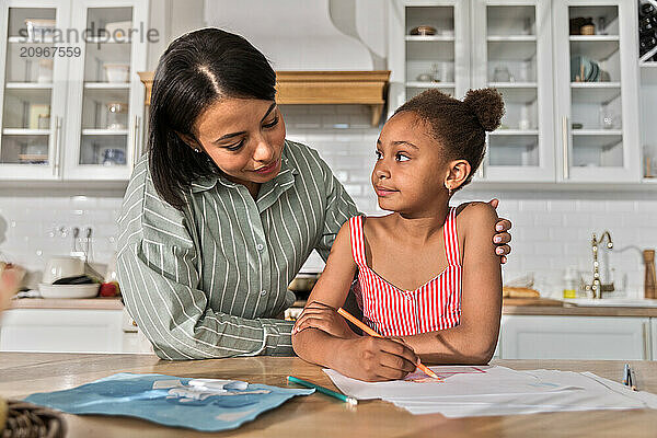 Afro woman and kid girl doing homework drawing on breakfast together