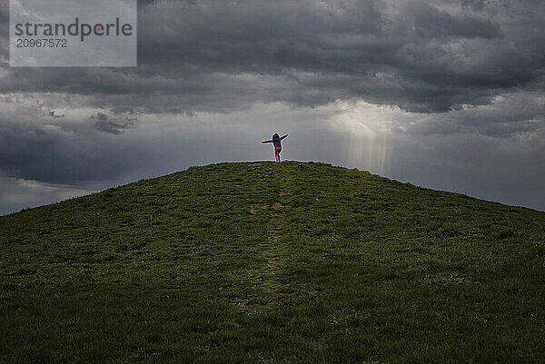 Young girl twirling on top of hill under stormy sky