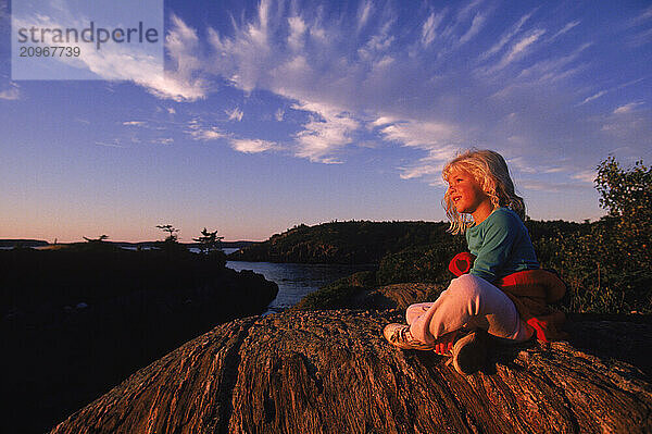 A young girl sits on a hill on Hermit Island  Maine.