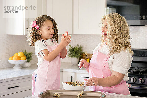 Daughter making dough in her hands while mother is smiling at her