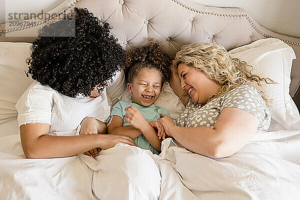 Sister and mother tickling little girl in bed