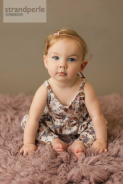 Baby girl in a cow print romper on a pink rug