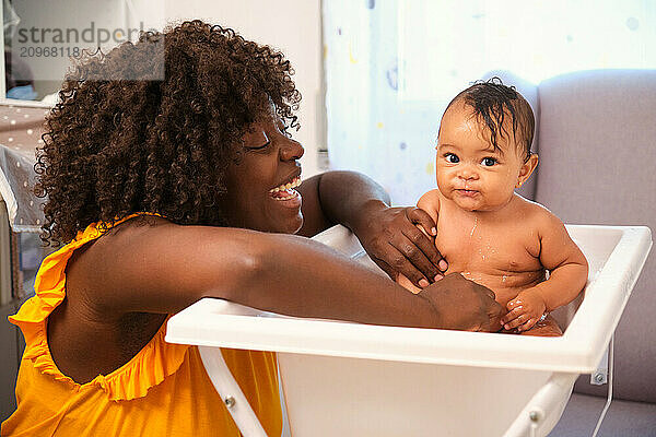 Happy mother washing her baby in a white bathtub