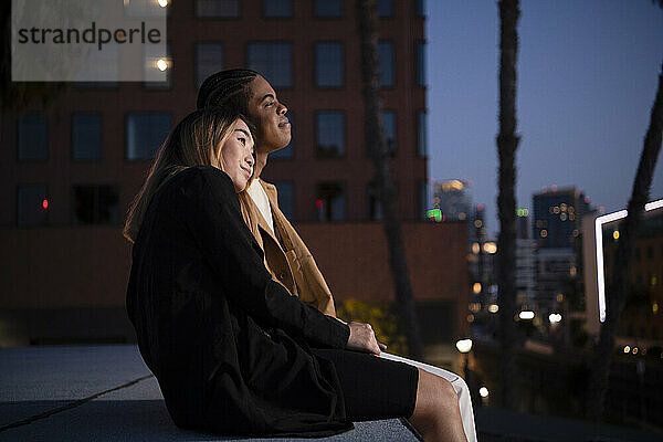 Multi racial couple snuggling embracing on urban rooftop at nigh