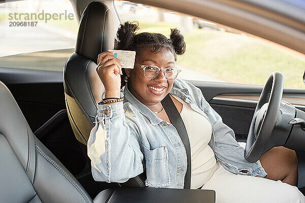 Young woman holding up a drivers license in a car