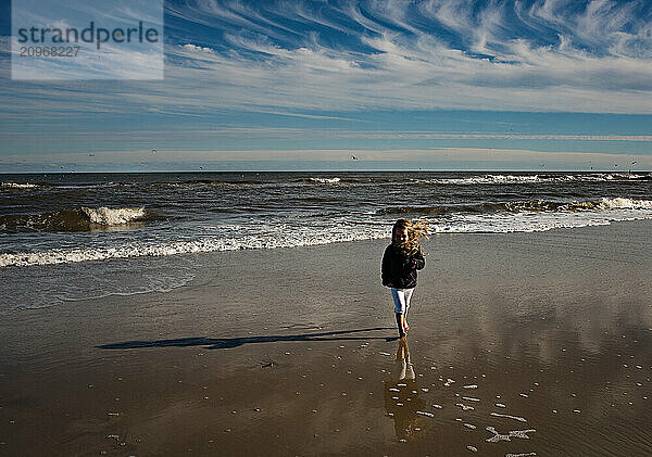 Young girl standing on windy beach under blue sky