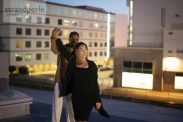 Black male and asian female dancing on an urban roof-top at nigh