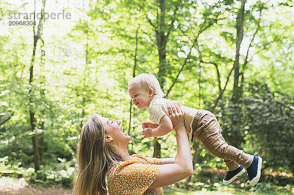 Mom smiles up at toddler as she holds him in the air.