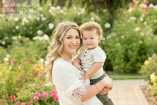 Mother holding baby son in garden smiling