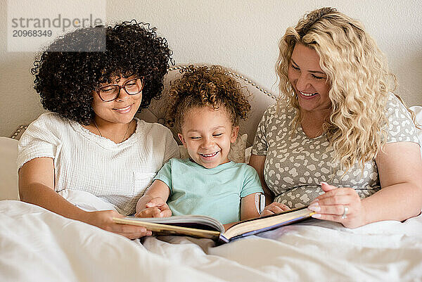 Mother and two daughters reading book in bed with all of them smilinga