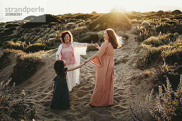 Happy white girl mom grandma 3 generations dancing beach sunset Spain