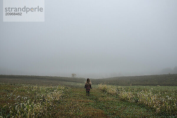 Young girl walking down foggy path in plaid coat