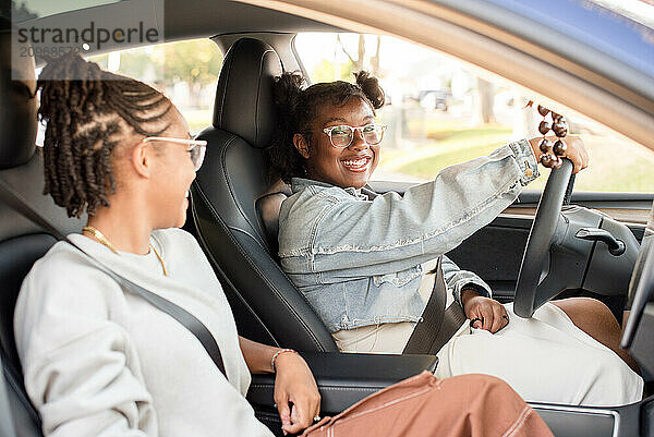 Young girl behind the steering wheel of a car with friend