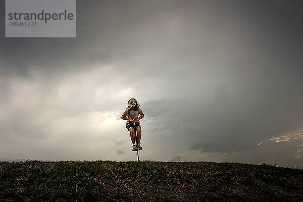 Young girl jumping on pogo stick on top of hill