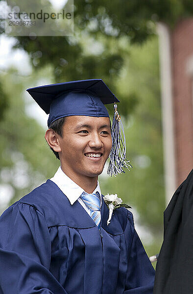 A young male student smiles as he receives his diploma during a high school graduation ceremony.