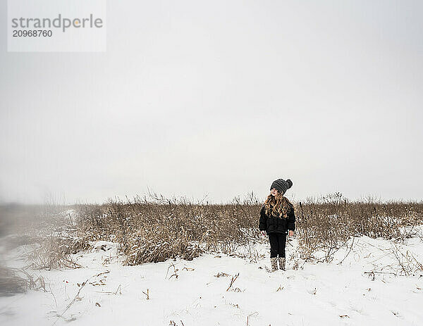 Young girl wearing knit hat standing in snow covered field