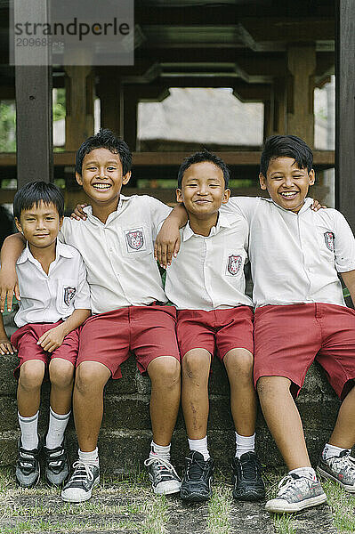 A group of young boys smiling and playing on an open field and climbing a tree