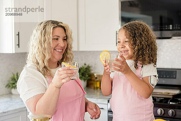 Mother and daughter holding glasses on lemonade in the kitchen