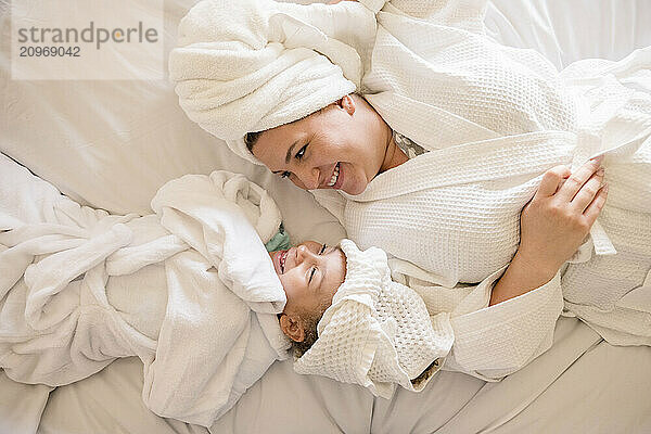 Mother and daughter smiling at each other laying on their back in bed