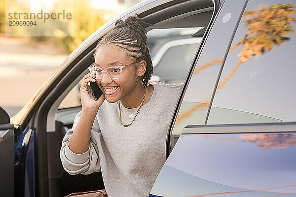 Young lady smiling talking on phone getting out of a car