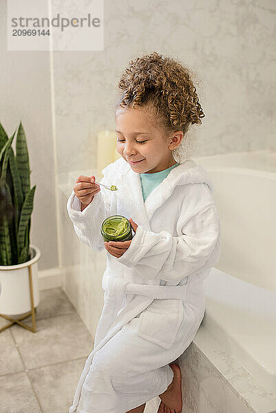 Little girl is holding avocado mask in the bathroom