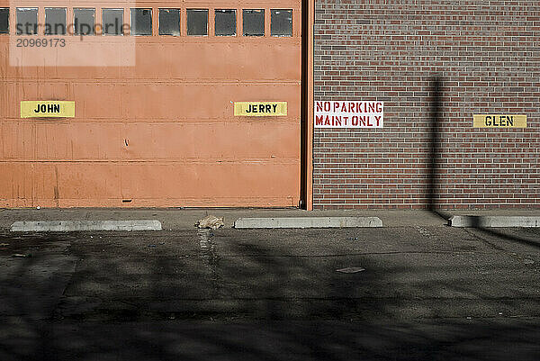 Assigned parking spaces are marked with name tags hung on a brick wall and a garage door.