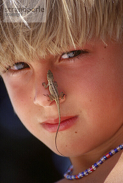 Close-up of boy with a lizard on his nose.