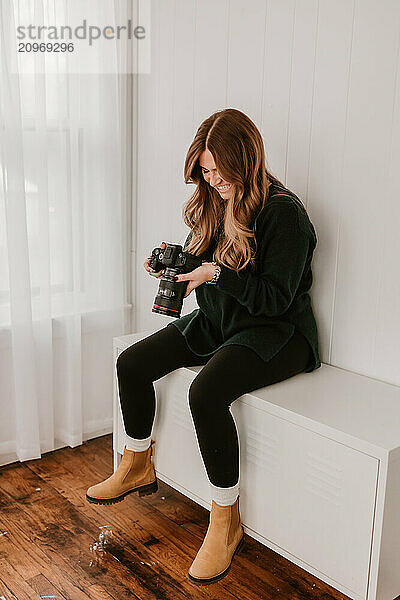 Smiling woman holding a camera  sitting on a white cabinet