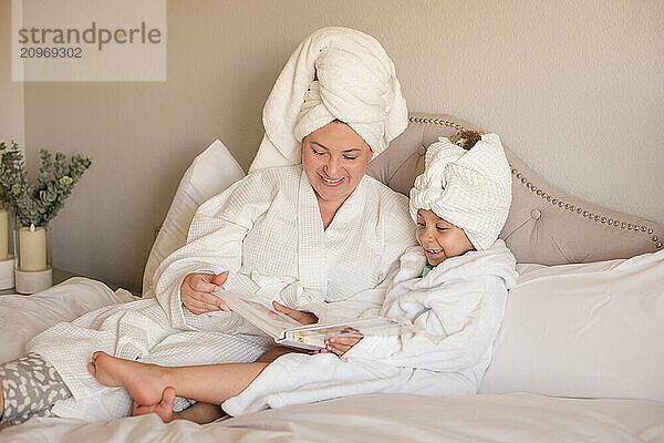 Mother and daughter are relaxing in bed reading a book